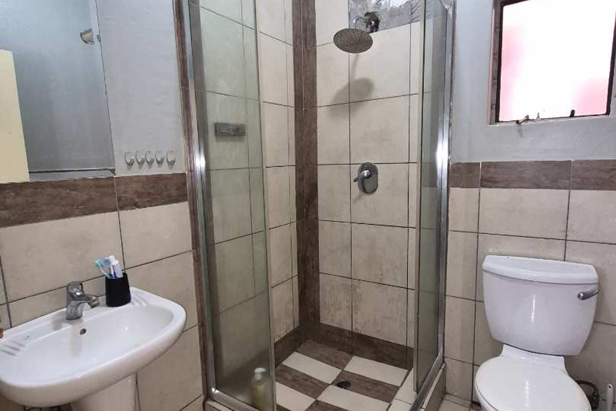 A functional bathroom featuring a pedestal basin, a glass-enclosed shower cubicle, and a standard toilet with tiled walls and flooring.