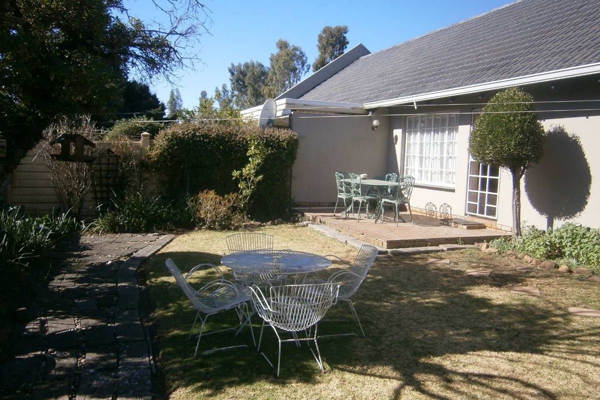A private rear garden featuring a paved patio area, stone pathway, and established boundary wall, providing a functional outdoor space for the townhouse.
