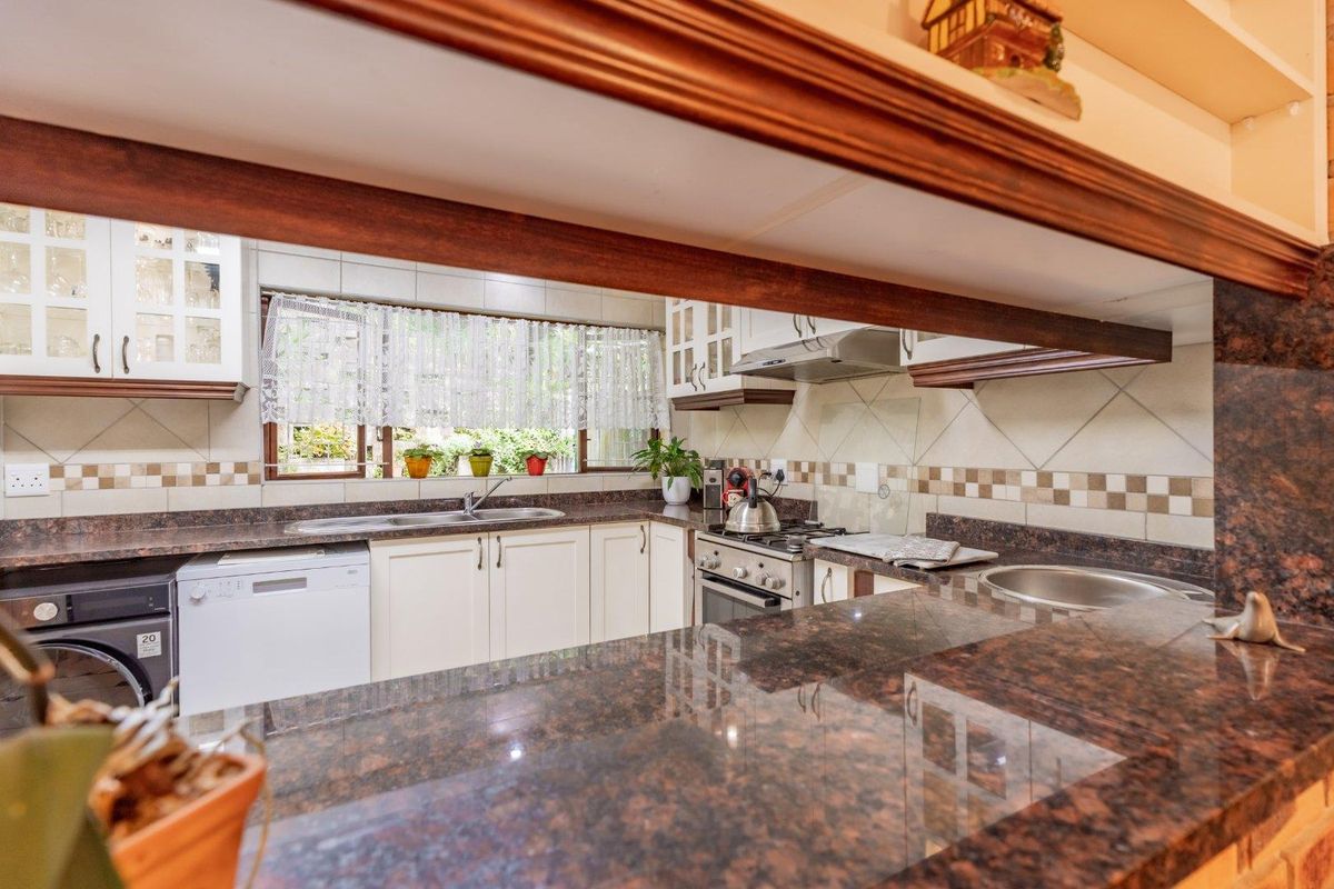 A functional kitchen featuring granite countertops, tiled backsplash, built-in cabinetry, a gas stove with extractor fan, and a double sink.