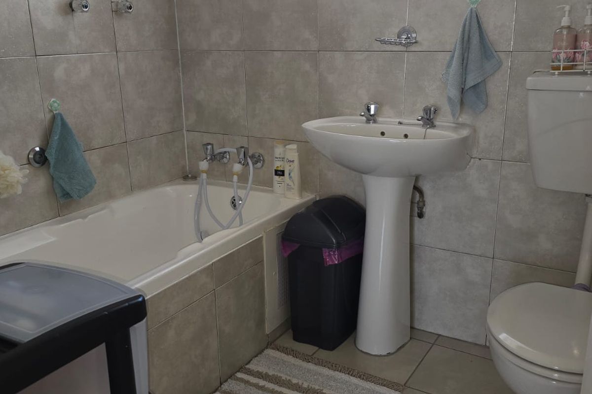A functional bathroom featuring a standard bathtub, pedestal basin, and toilet with neutral wall tiling.
