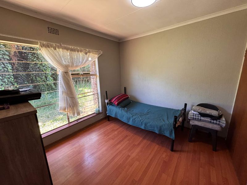 A bedroom featuring laminate flooring, built-in cupboards, and large windows with security bars, offering a functional space ready for cosmetic updates.