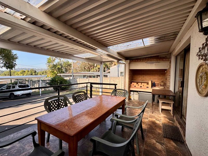 Covered patio area featuring a built-in brick braai, tiled flooring, and metal railing, providing an outdoor space for entertaining.