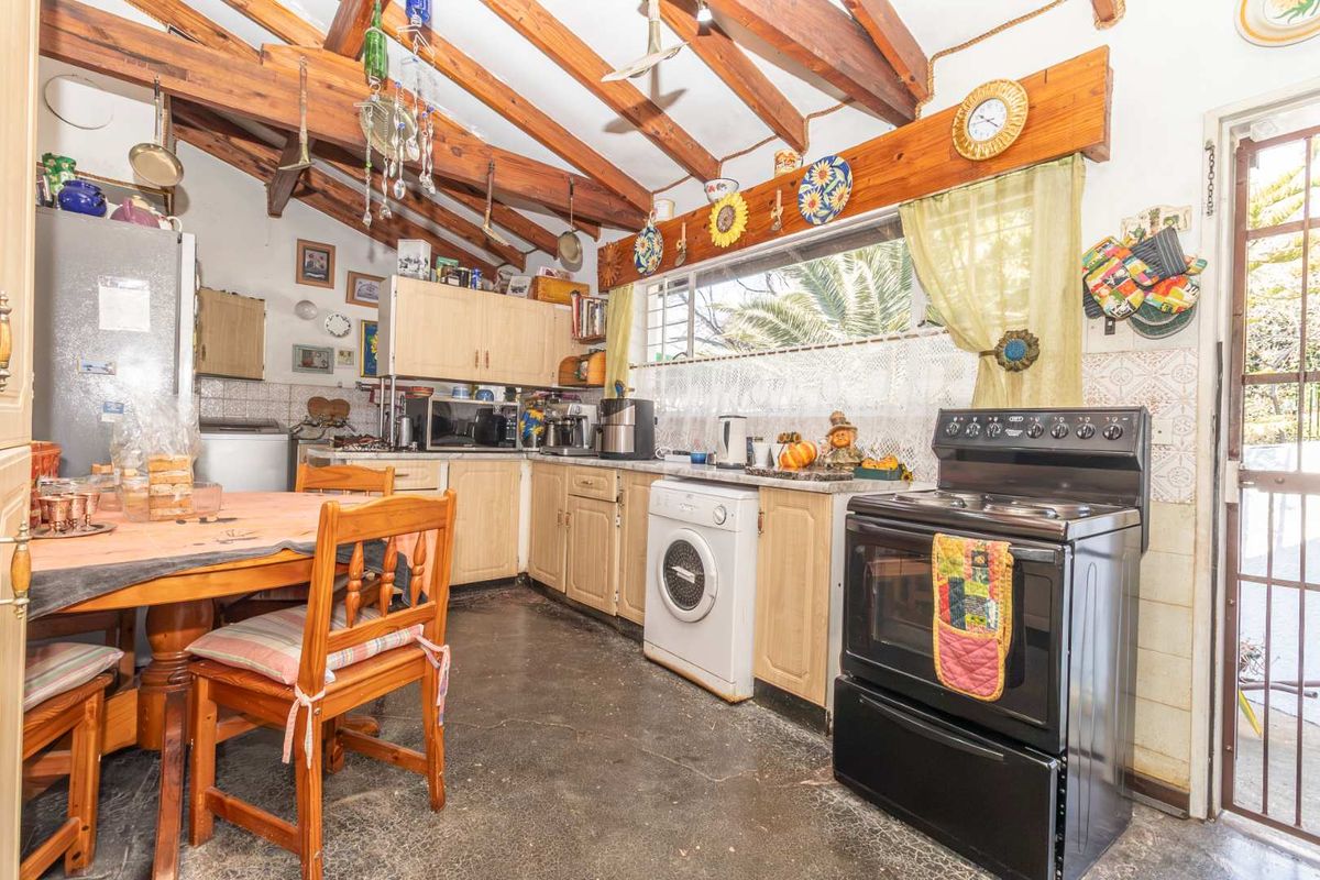 A rustic kitchen featuring exposed timber rafters, laminate cabinetry, and a freestanding oven, with direct access to the exterior.