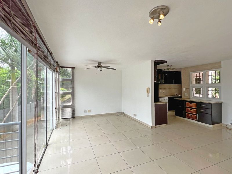 Spacious open-plan living area featuring tiled floors, a ceiling fan, and large sliding glass doors leading to the exterior, adjacent to a fitted kitchen.