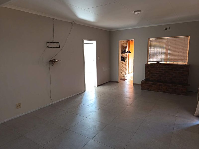 An empty living room featuring tiled flooring and a brick fireplace hearth, requiring minor cosmetic repairs to wall surfaces and electrical fixtures.