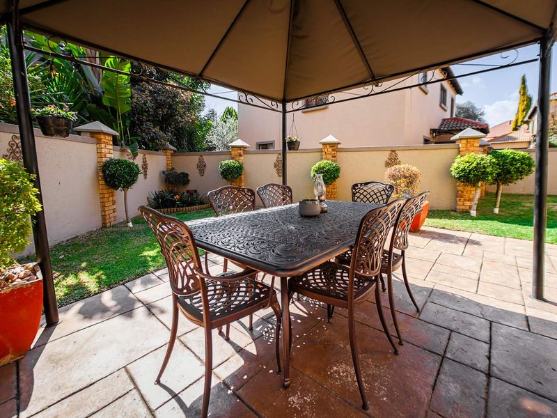 A well-maintained paved patio area featuring a covered outdoor dining space, enclosed by a perimeter wall with decorative brick pillars and a landscaped garden.