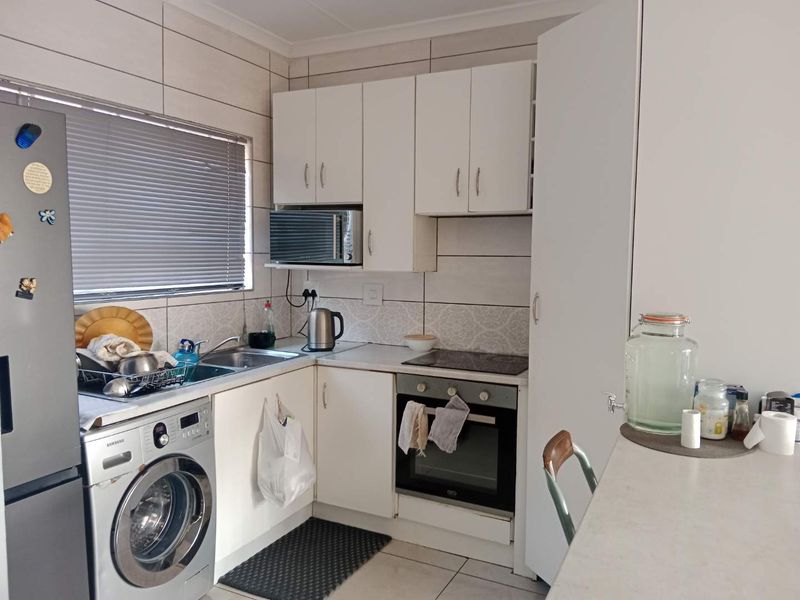 Compact kitchen featuring white cabinetry, built-in oven and hob, tiled backsplash, and integrated laundry plumbing, offering a functional layout for an apartment.