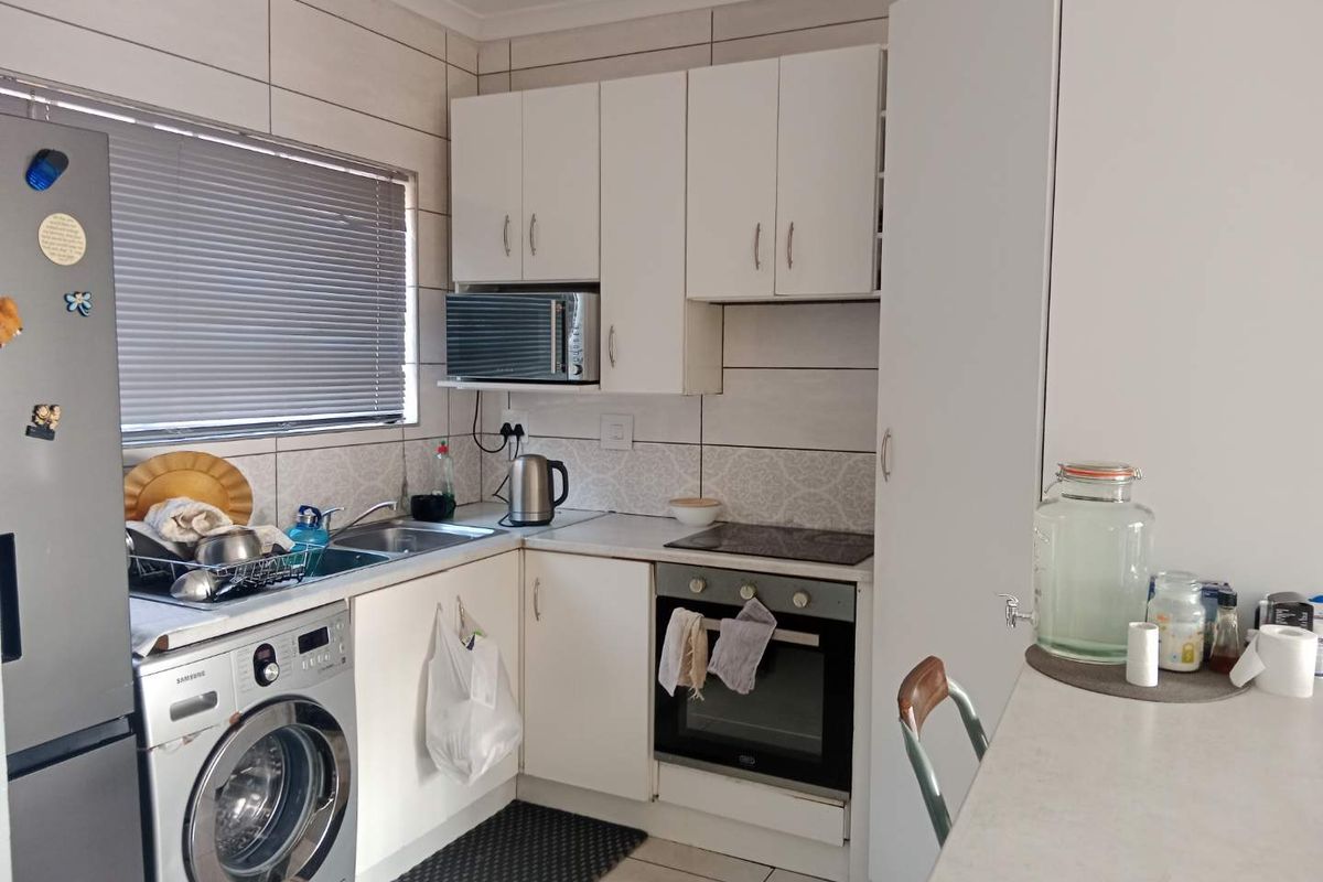 Compact kitchen featuring white cabinetry, built-in oven and hob, tiled backsplash, and integrated laundry plumbing, offering a functional layout for an apartment.