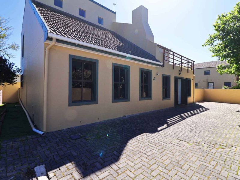 Rear view of the property featuring a paved courtyard, tiled roof, and an upper-level balcony with wooden railings.