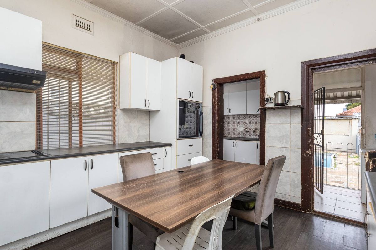 A dated kitchen featuring built-in cabinetry, an integrated oven, and a tiled splashback, with direct access to a scullery and outdoor area.