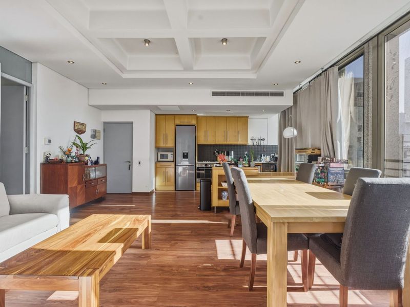 Spacious open-plan living and dining area featuring wooden flooring, a coffered ceiling, and a modern kitchen with integrated appliances and ample cabinetry.