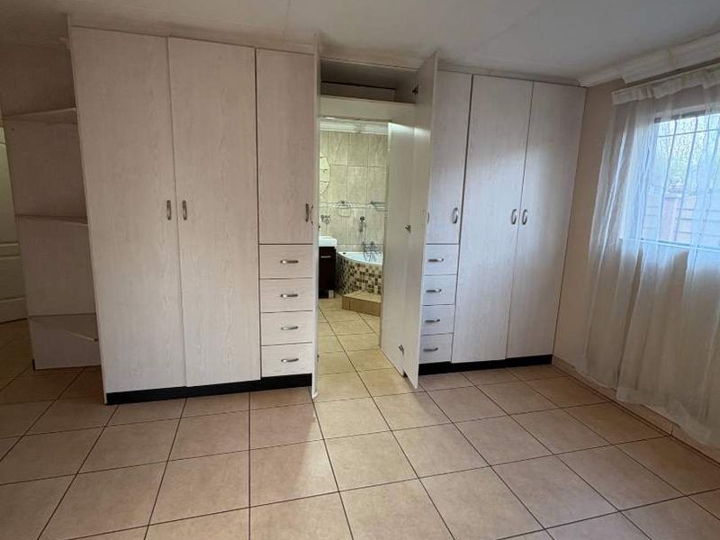 A spacious bedroom featuring neutral tiled flooring, extensive built-in cabinetry, and direct access to an en-suite bathroom.