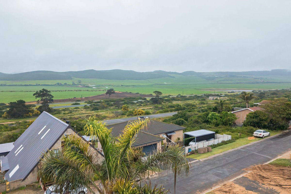 An elevated aerial view of a residential neighborhood featuring tiled and metal roof structures, paved driveways, and expansive green landscape views.