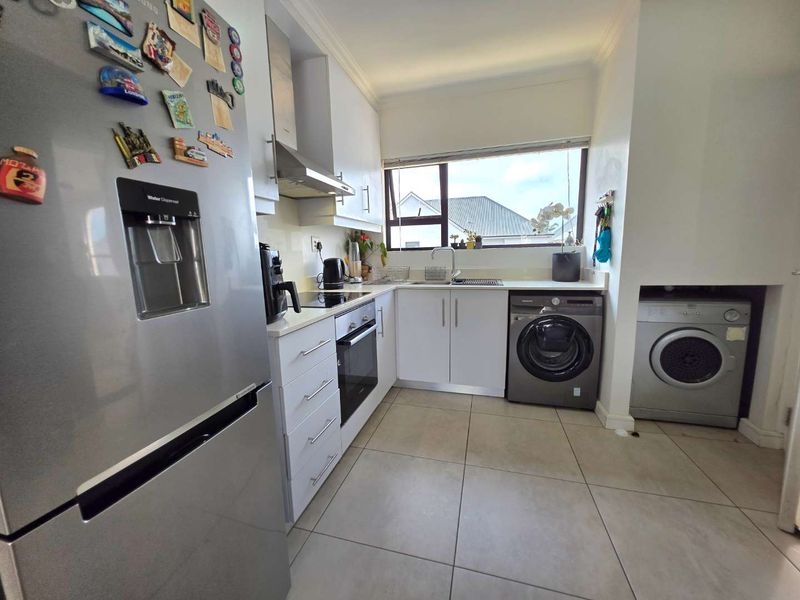 A functional kitchen featuring white cabinetry, built-in oven and hob, stainless steel extractor fan, and dedicated space for laundry appliances.