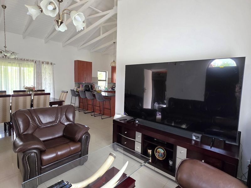 Spacious open-plan living and dining area featuring vaulted ceilings with exposed rafters, tiled flooring, and a functional kitchen with a central island.