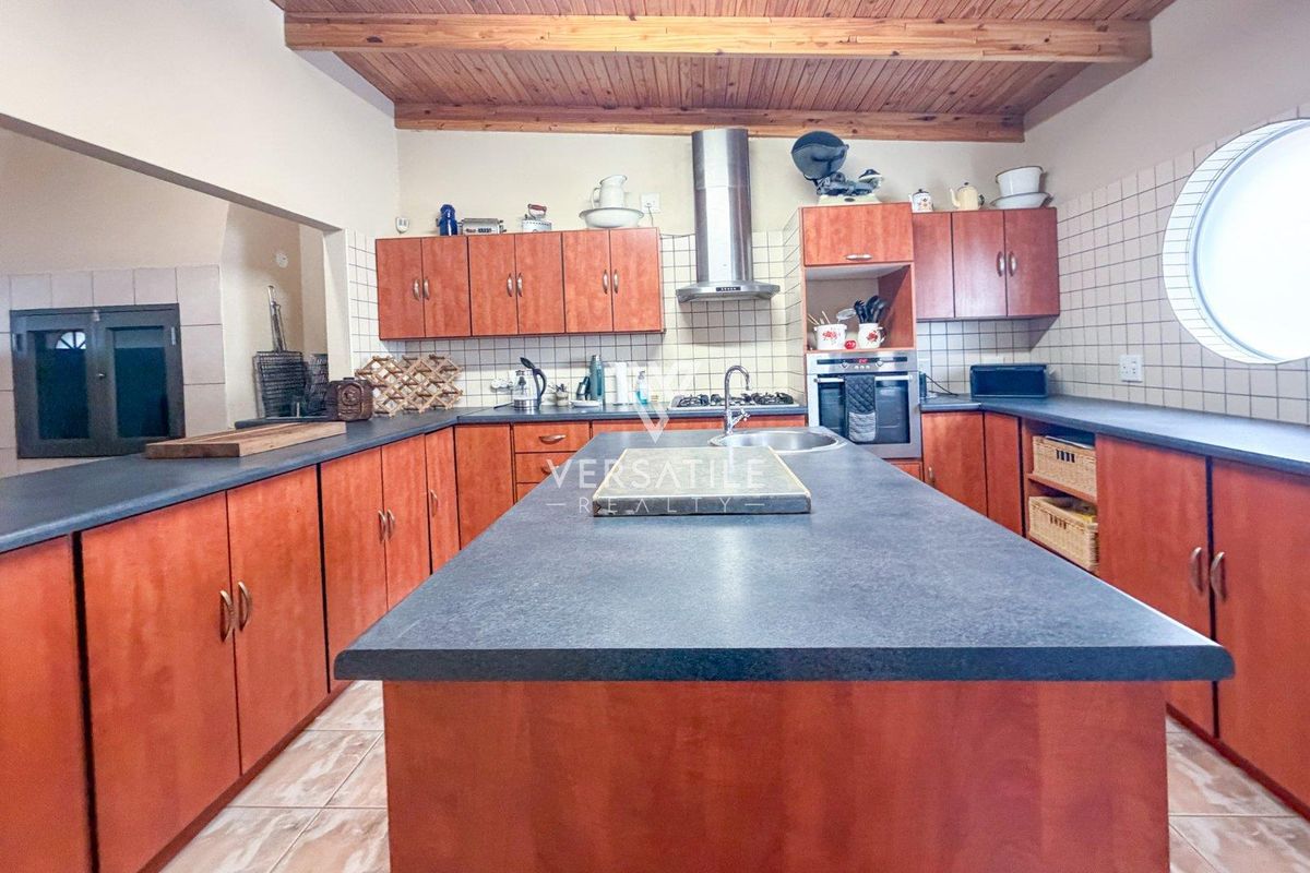 Spacious kitchen featuring a central island, timber ceiling, built-in oven, gas hob, extractor fan, and ample cabinetry with dark countertops.