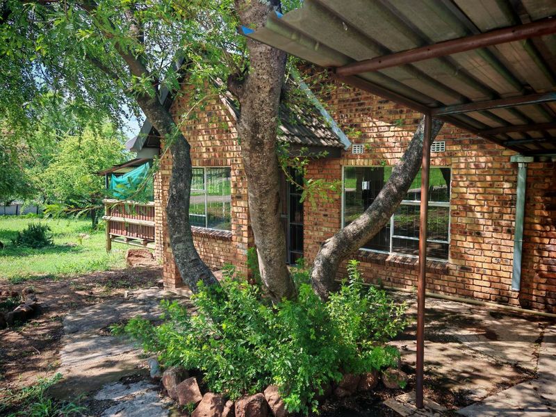 Rear view of a face brick house featuring a paved patio area, metal carport structure, and established garden surroundings.