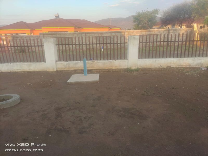 A rear yard area featuring a concrete boundary wall with metal palisade fencing and an exposed concrete plinth on unlandscaped ground.