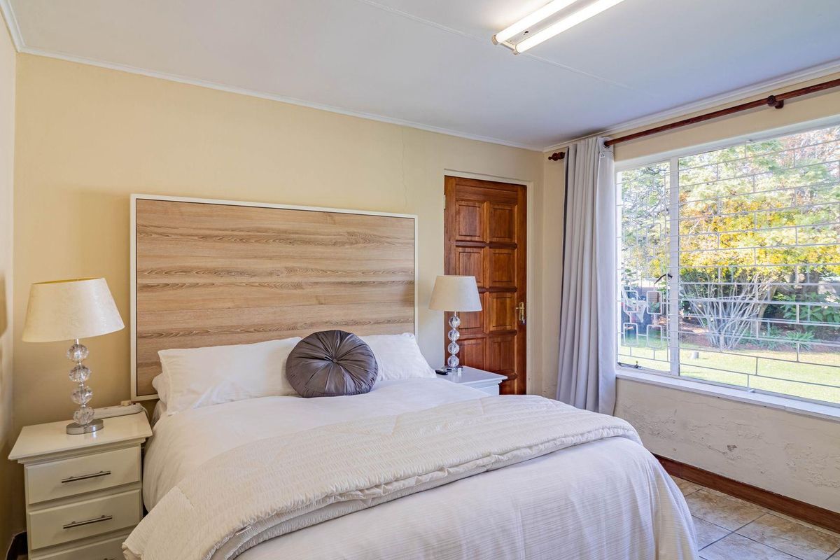A bedroom featuring a large window with security bars, a wooden door, and tiled flooring.