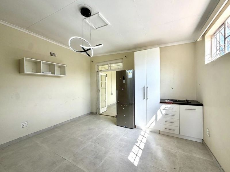 A compact kitchen area featuring tiled flooring, built-in white cabinetry, and a modern pendant light fixture, offering a functional and clean space.