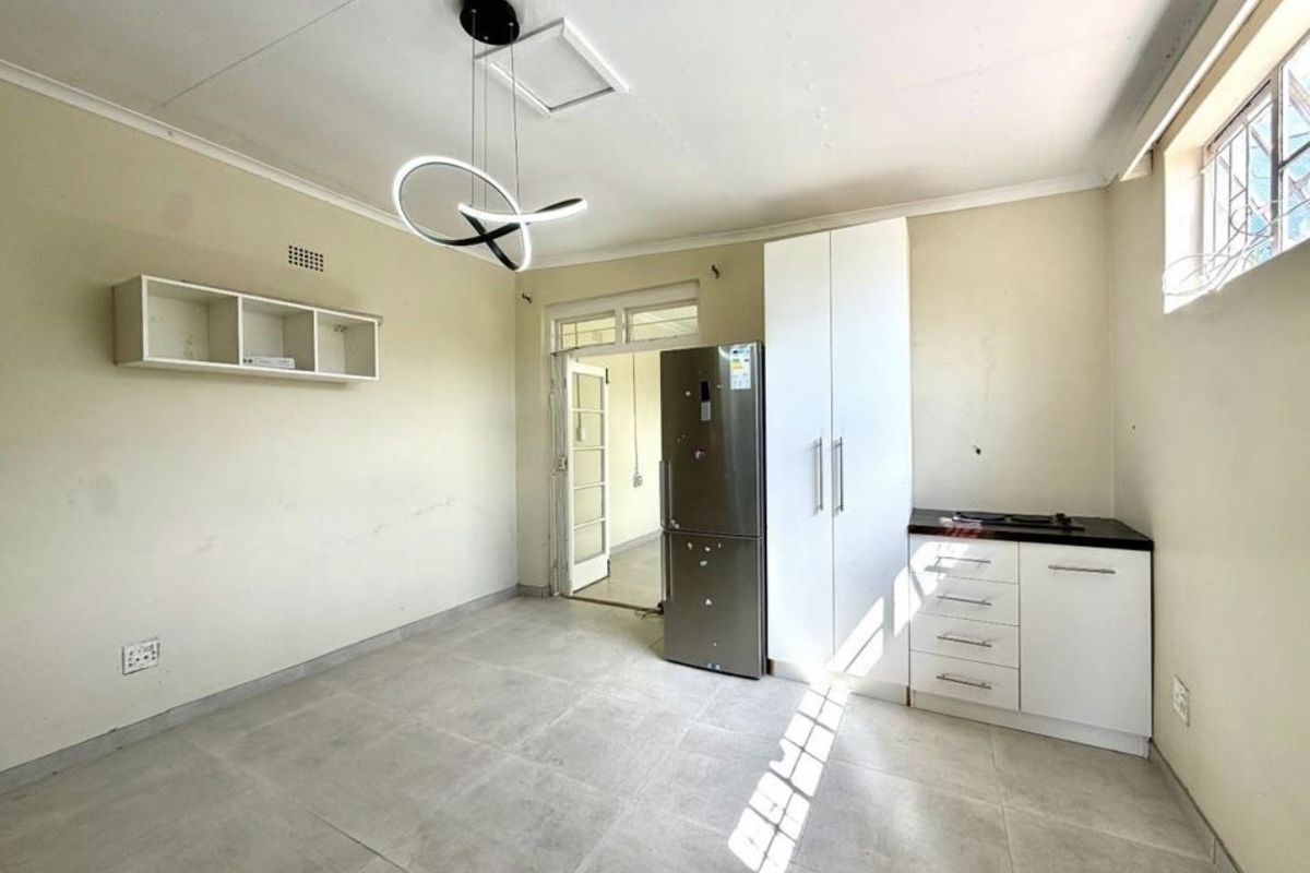 A compact kitchen area featuring tiled flooring, built-in white cabinetry, and a modern pendant light fixture, offering a functional and clean space.