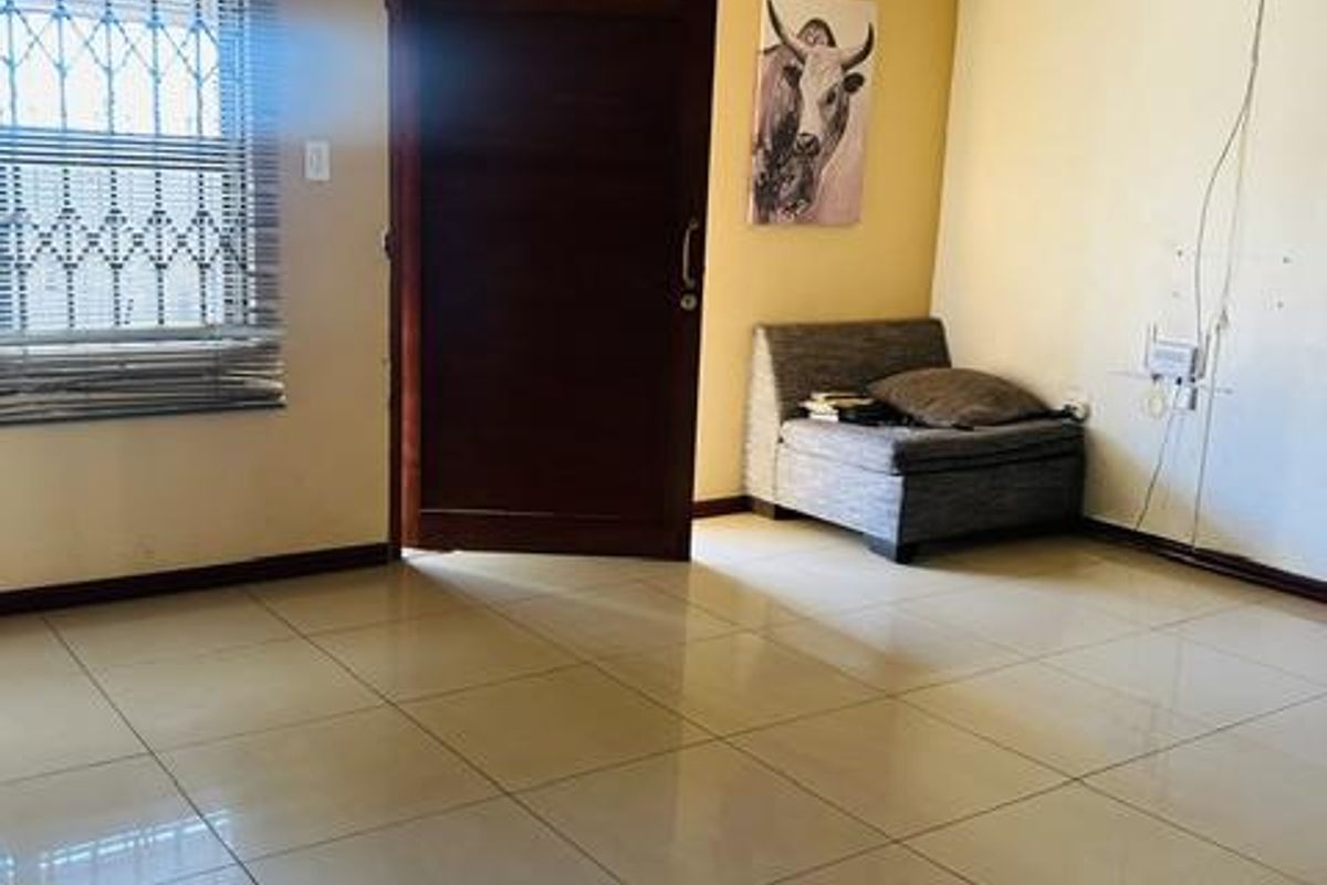 Spacious living area featuring tiled flooring, a decorative recessed ceiling tray, and security window treatments. The room is ready for personalization.