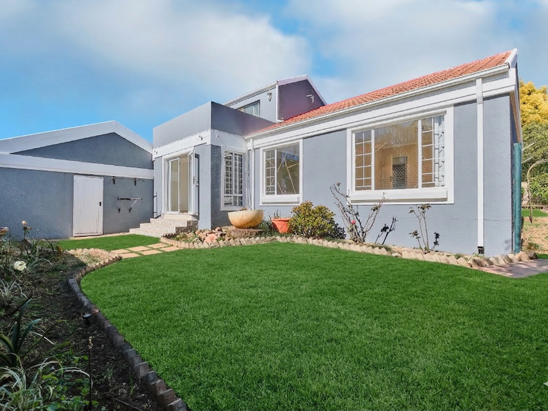 Rear view of the property featuring a well-maintained lawn, landscaped garden beds, and a paved pathway leading to the house entrance.