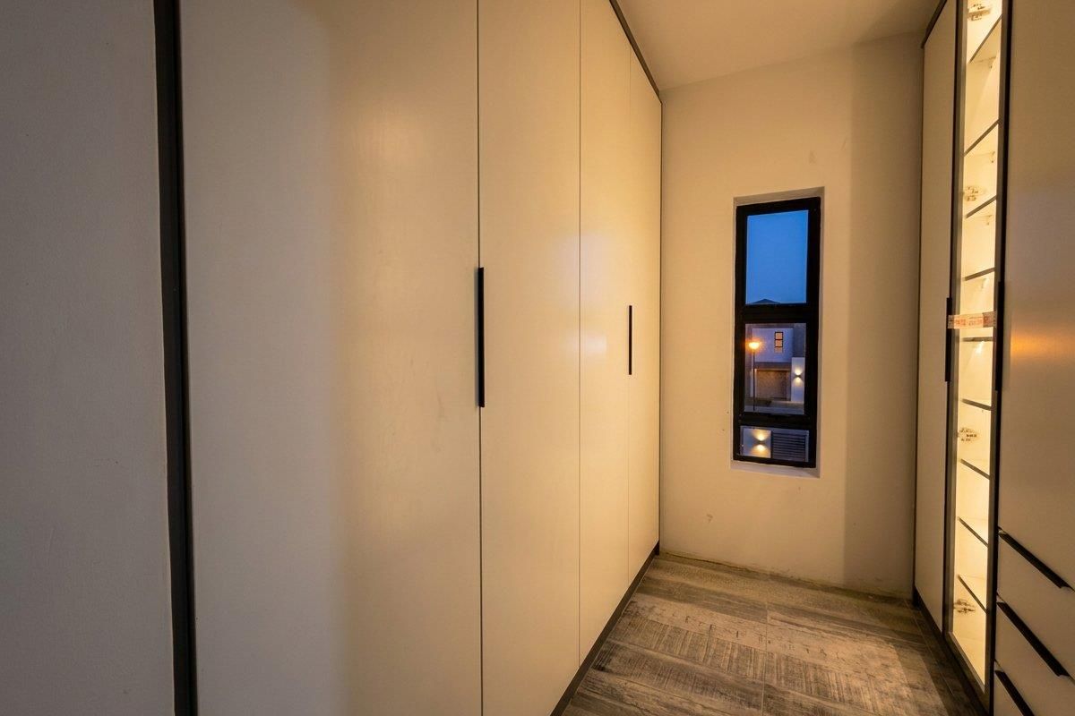 A modern walk-in closet or dressing area featuring floor-to-ceiling built-in cupboards, tiled flooring, and a vertical window providing natural light.