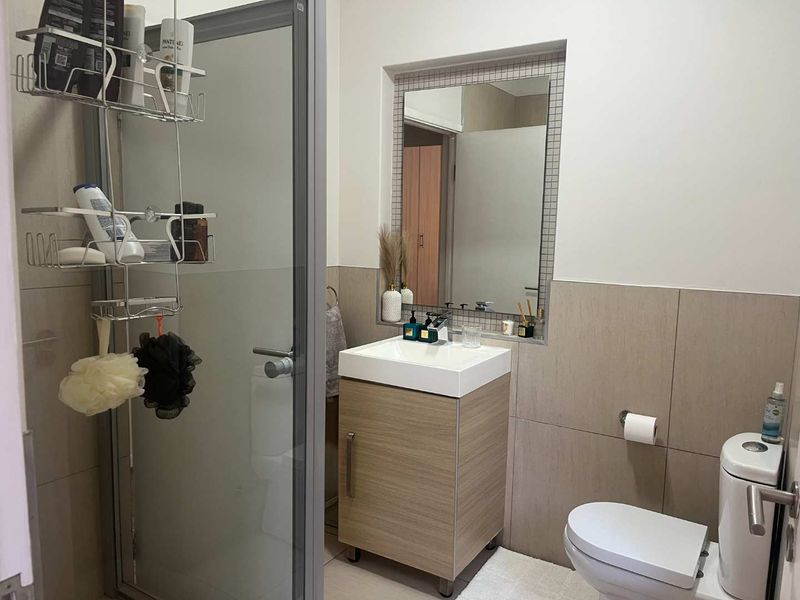 A modern bathroom featuring a vanity cabinet with basin, a toilet, and a glass-enclosed shower with neutral wall tiling.