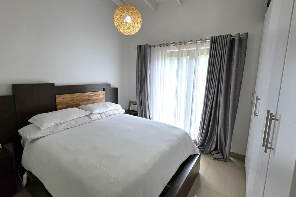A bright bedroom featuring a vaulted ceiling, tiled flooring, built-in wardrobe, and a sliding glass door providing access to the outdoors.