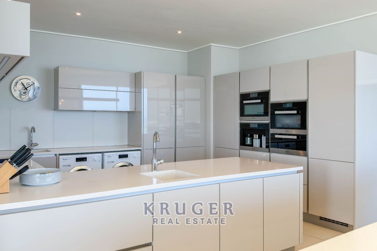 Modern kitchen featuring high-gloss cabinetry, stone countertops, a central island, and integrated high-end appliances in a sleek, contemporary penthouse setting.
