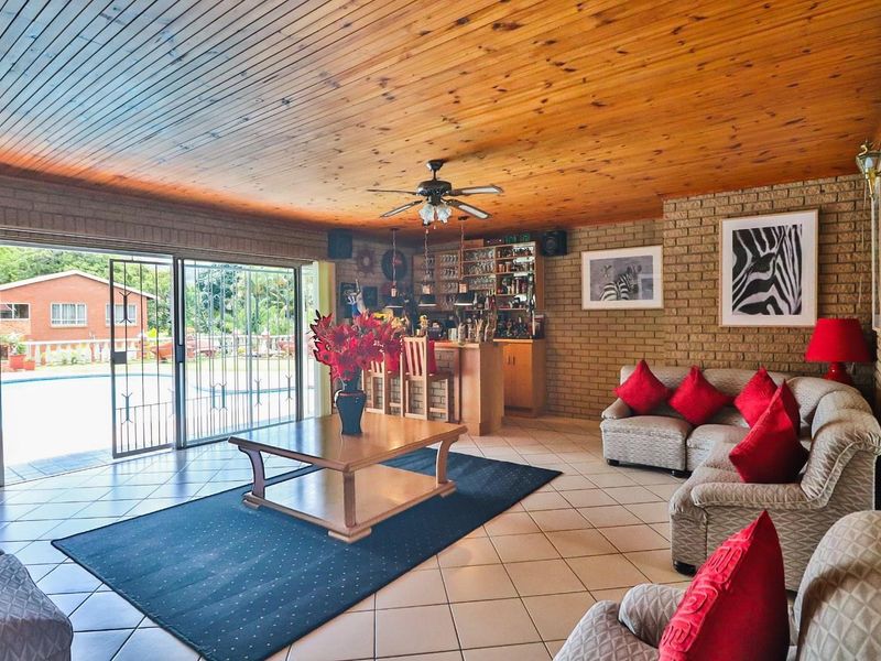 Spacious open-plan living area featuring a timber-clad ceiling, exposed brick walls, a built-in bar, and sliding doors opening to the pool area.