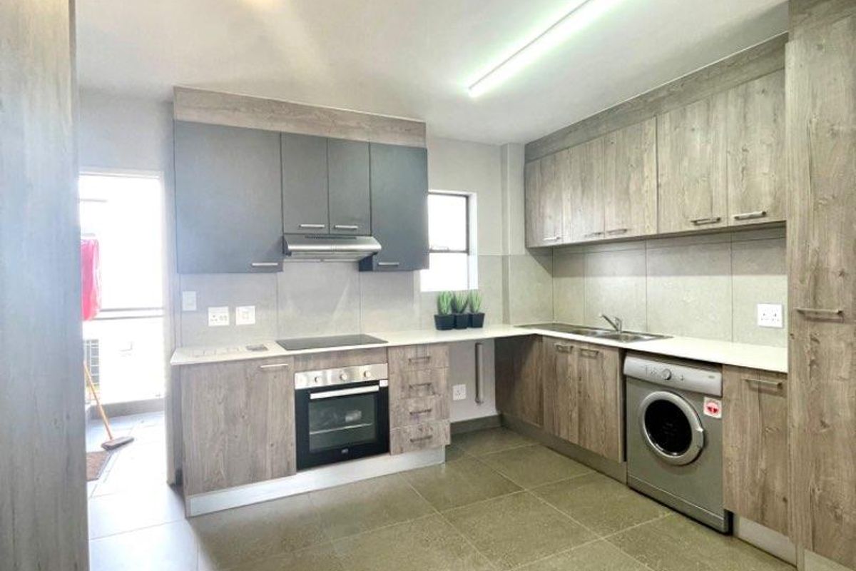 Modern kitchen featuring wood-grain cabinetry, stone countertops, integrated oven, hob, extractor fan, and space for a washing machine.