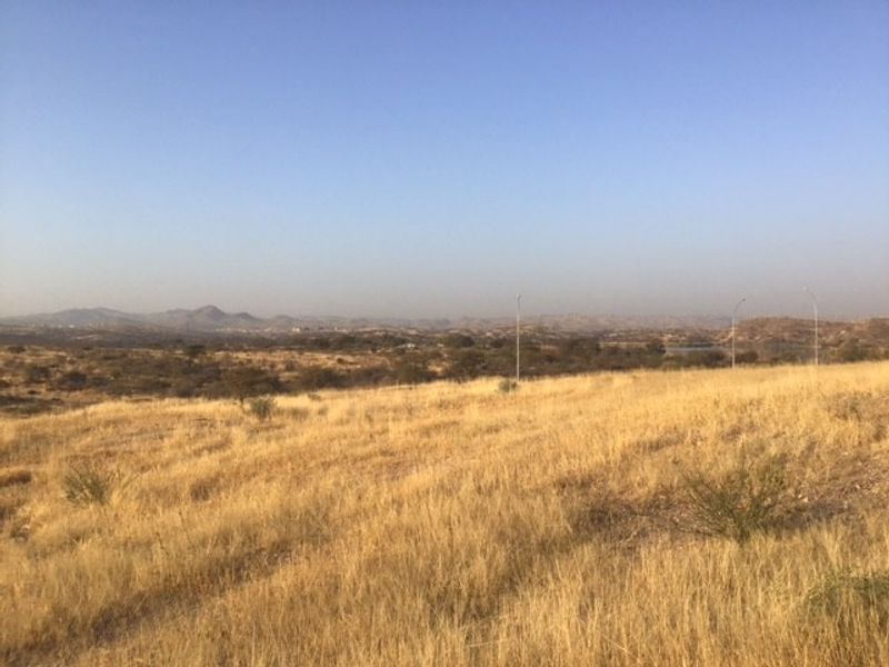 A wide-angle view of the vacant residential land featuring dry grass and distant hilly landscape.