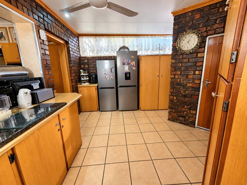 A kitchen featuring exposed brick walls, ceramic tiled flooring, laminate cabinetry, and granite countertops, offering a rustic aesthetic with functional storage space.