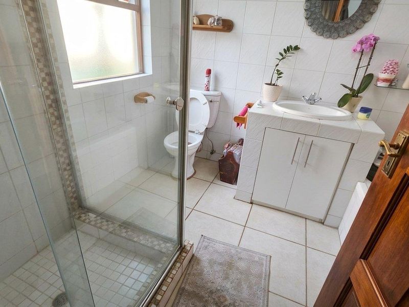 A functional bathroom featuring a glass shower enclosure, a tiled vanity with a basin, and a toilet, finished with neutral wall and floor tiles.