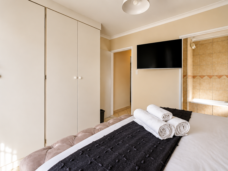A well-maintained bedroom featuring ample built-in cupboard storage, a wall-mounted television, and direct access to an en-suite bathroom with tiled finishes.