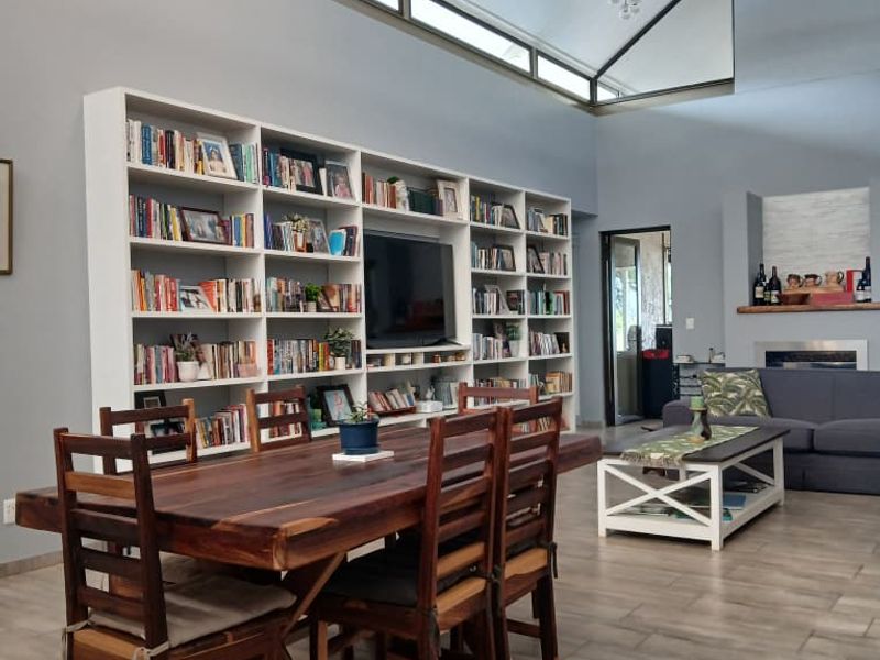 Spacious open-plan living and dining area featuring a vaulted ceiling, clerestory windows, a large built-in bookshelf, and a fireplace.