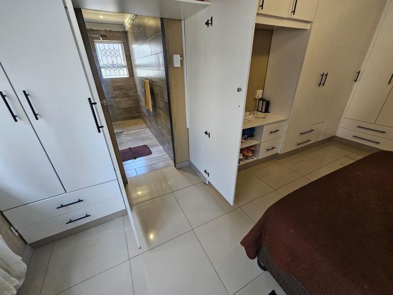A well-maintained bedroom featuring extensive built-in cabinetry, neutral tiled flooring, and direct access to an en-suite bathroom with modern finishes.