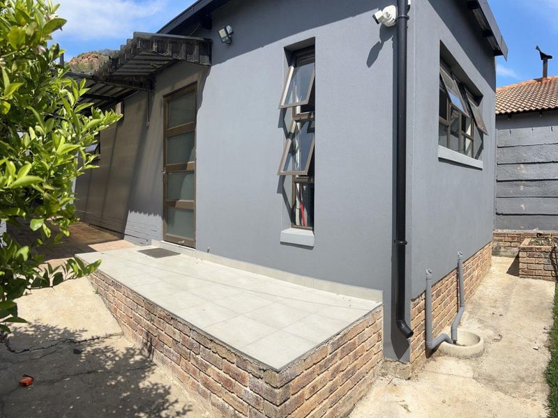 Rear exterior view of the apartment featuring a raised tiled patio, brick foundation, and modern grey painted facade with top-hung windows.