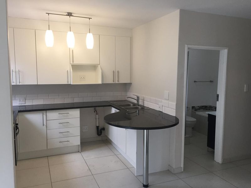 A clean, modern kitchen featuring white cabinetry, black granite countertops, a breakfast bar, and a subway tile backsplash, with an adjacent bathroom entrance.