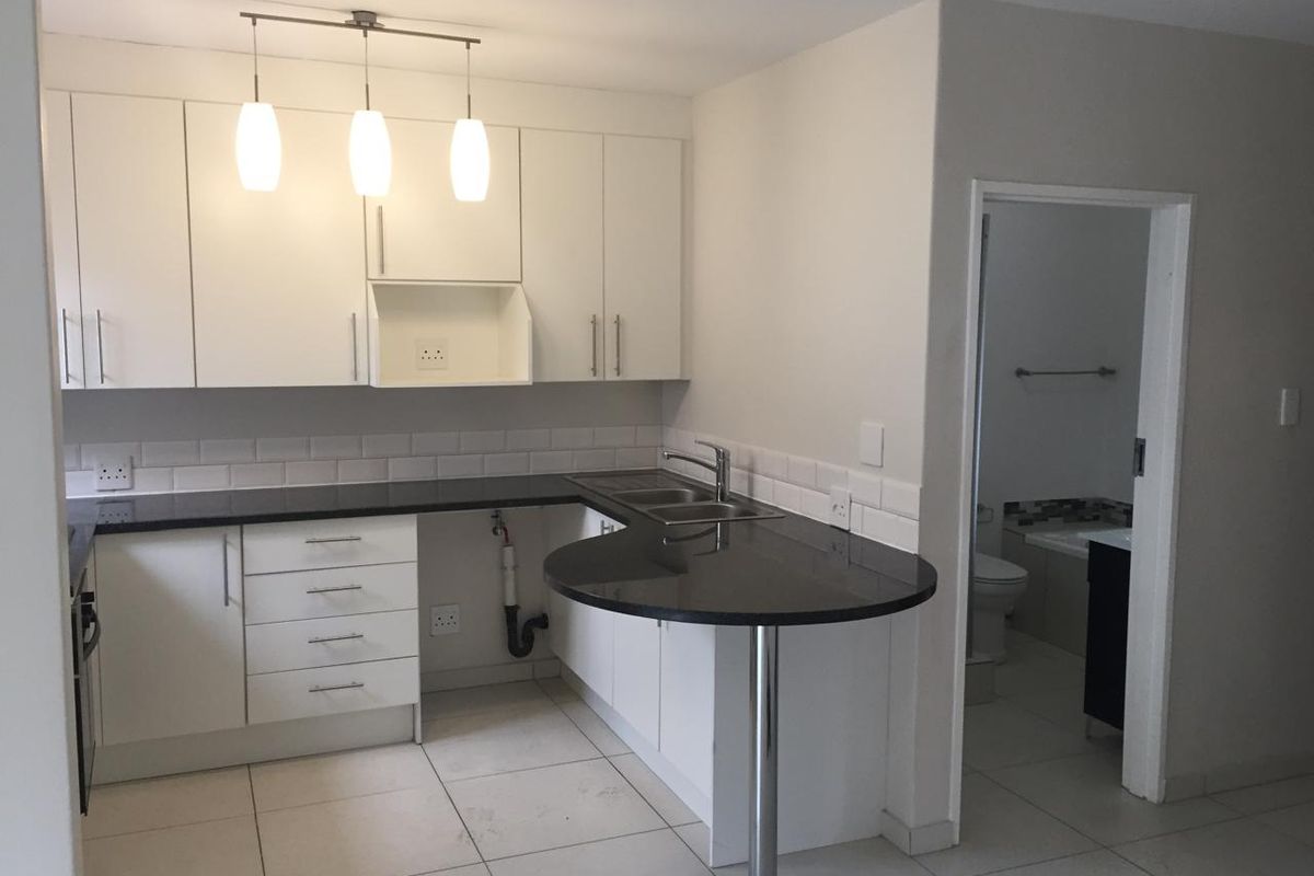 A clean, modern kitchen featuring white cabinetry, black granite countertops, a breakfast bar, and a subway tile backsplash, with an adjacent bathroom entrance.