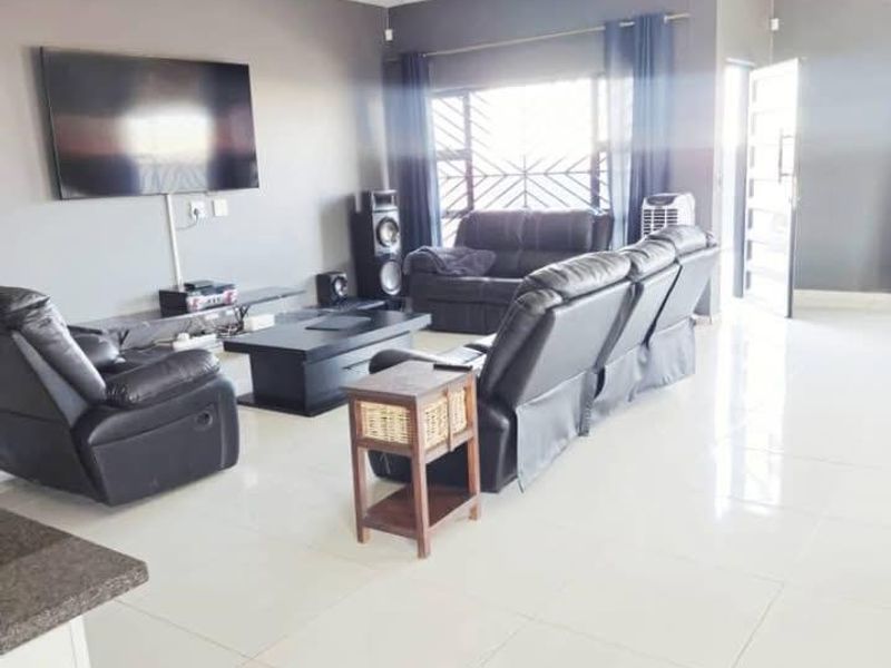 Spacious living room featuring large format floor tiles, neutral grey walls, and natural light through a window with security bars.