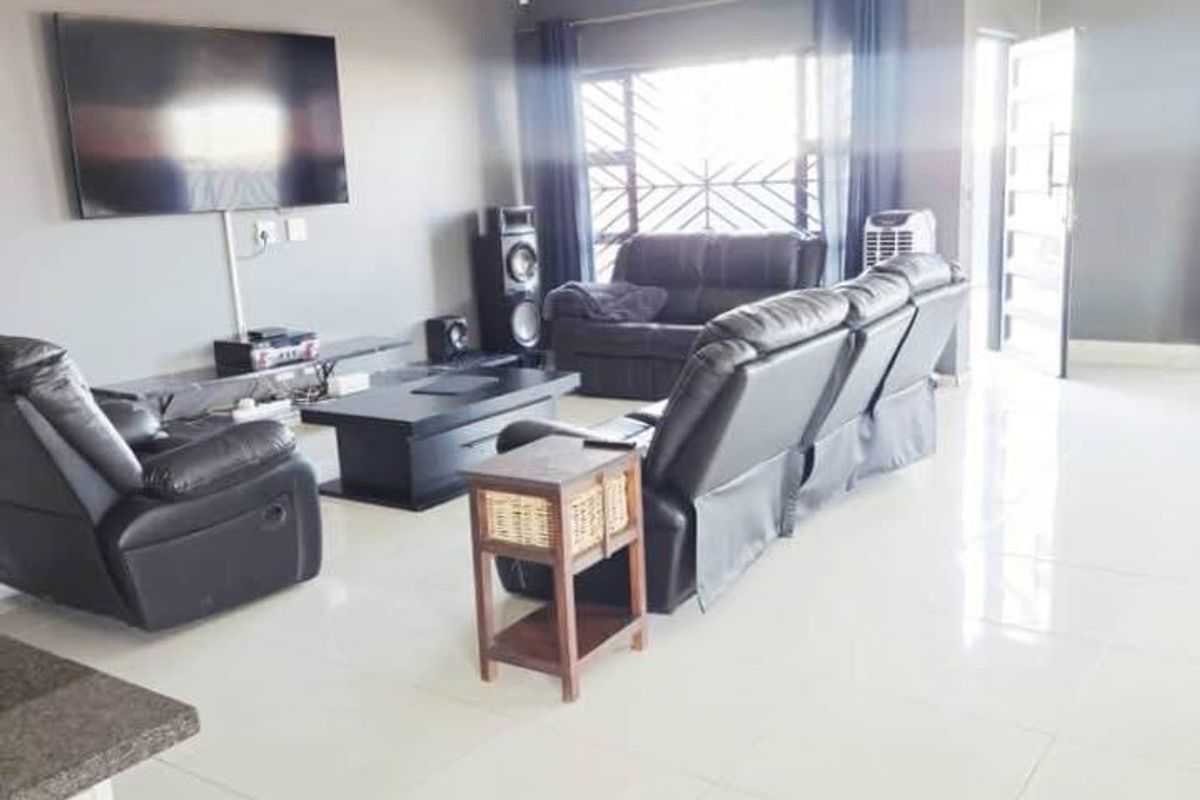 Spacious living room featuring large format floor tiles, neutral grey walls, and natural light through a window with security bars.
