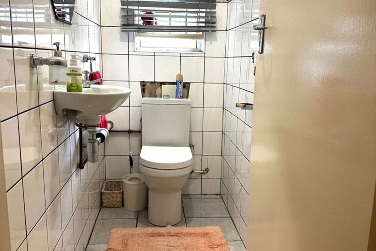 A compact bathroom featuring a wall-mounted basin and toilet, finished with floor-to-ceiling white wall tiles and a window with a venetian blind.