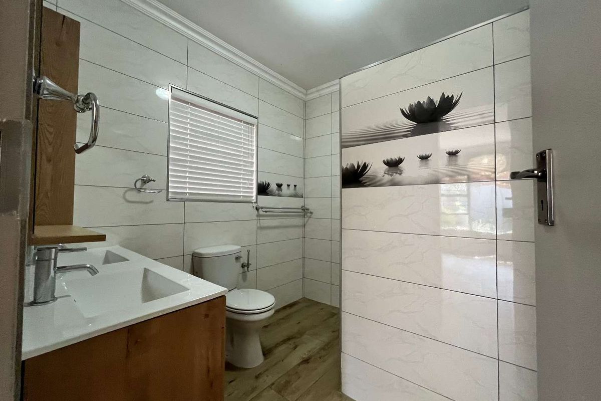 A modern bathroom featuring wood-look floor tiles, a vanity with basin, a toilet, and decorative wall tiling with a floral motif.