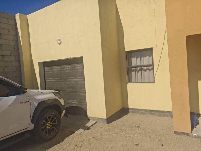 Front elevation of the property featuring a single garage door and a window, with an unpaved driveway area.