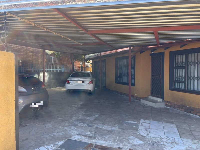 A covered carport area featuring a corrugated metal roof, steel support structure, and paved flooring, providing sheltered parking space.