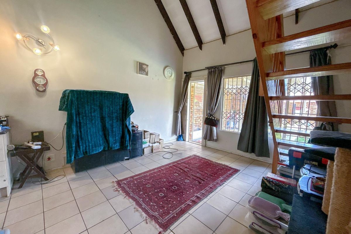 Open plan living area featuring vaulted ceilings with exposed timber beams, tiled flooring, and a wooden staircase leading to the upper level.