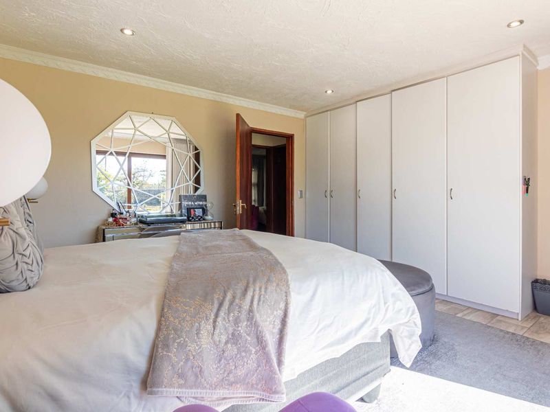 A well-maintained bedroom featuring extensive built-in cupboards, recessed downlighting, and neutral tiled flooring.
